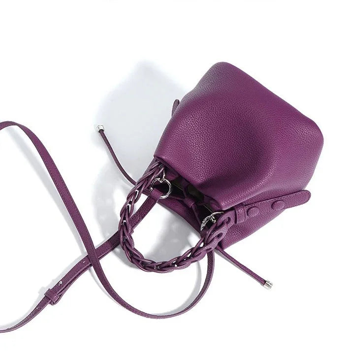 Purple leather bucket bag with braided handle and adjustable strap on white background