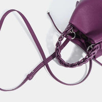 Purple leather crossbody bag with braided handle on white background