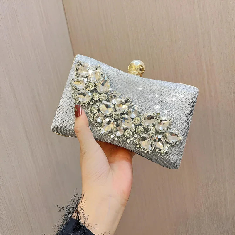 Hand holding a silver rhinestone clutch purse with crystal embellishments and gold clasp