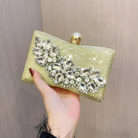 Hand holding a gold clutch purse with sparkling crystal rhinestone embellishments