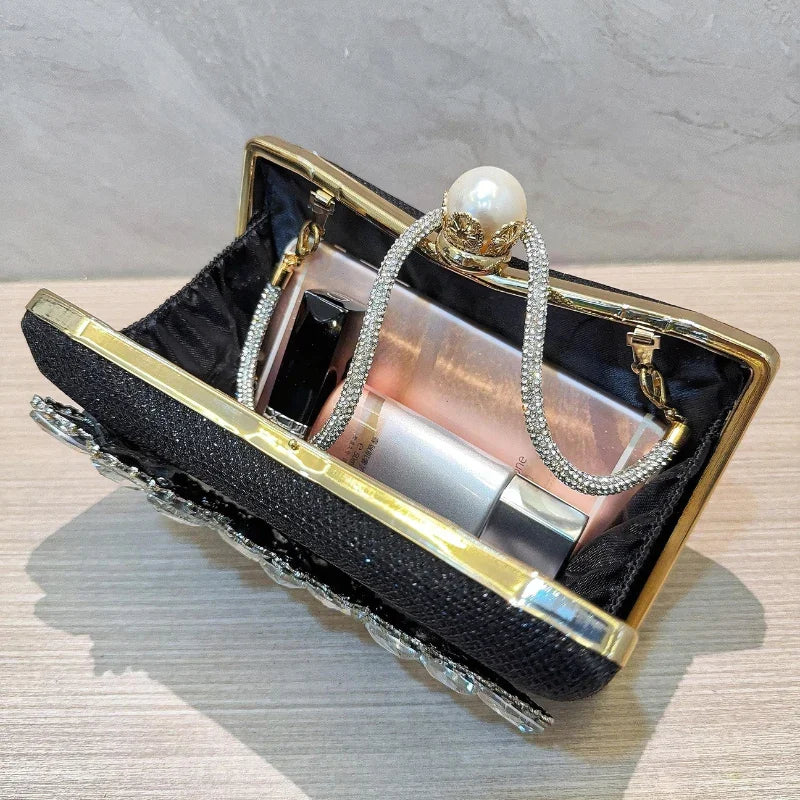 Black clutch purse with gold trim, pearl clasp, rhinestone handle, and cosmetics inside