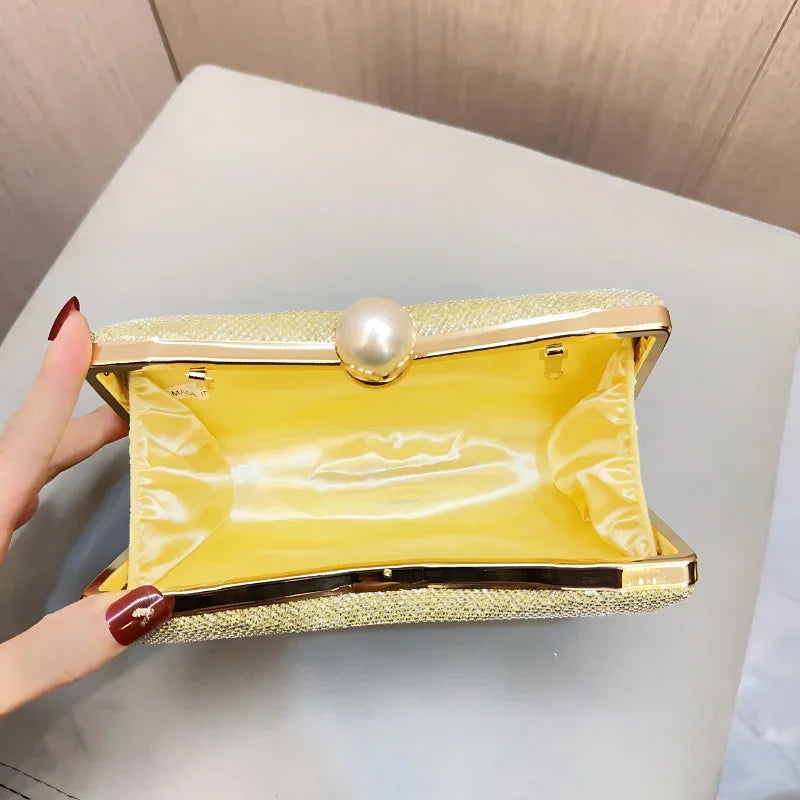 Open gold clutch purse with yellow satin lining and pearl clasp on gray surface