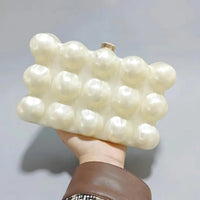 Hand holding a pearl bubble clutch bag with textured, glossy spheres against a plain background