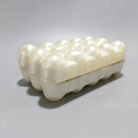 Pearl white clamshell handbag with bubble texture on a gray background