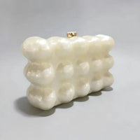 White pearl acrylic bubble clutch purse with gold clasp on a light gray background