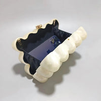 Pearl shell-shaped clutch purse open with a smartphone inside on a gray background