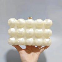 Hand holding a pearl bubble texture clutch purse against a plain background