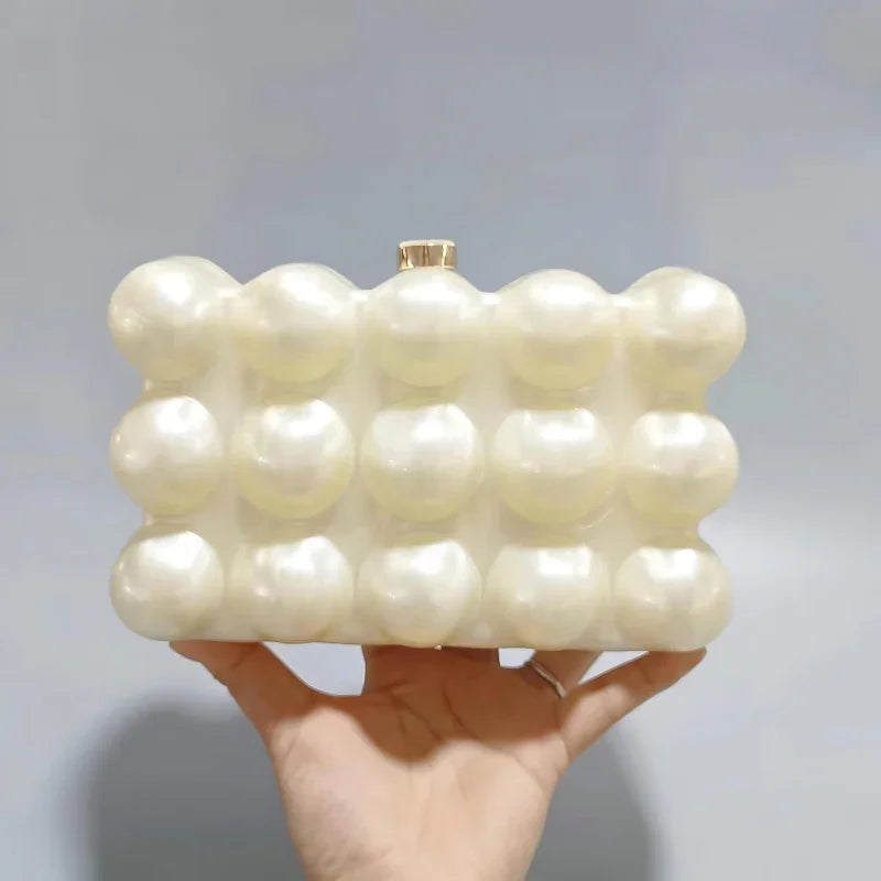 Hand holding a pearl bubble texture clutch purse against a plain background