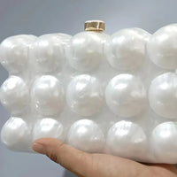 Hand holding pearl bubble clutch bag with gold clasp against neutral background