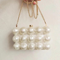 Pearl beaded clutch purse with gold chain strap held against a light background