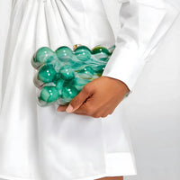 Woman in white dress holding a unique green bubble clutch bag