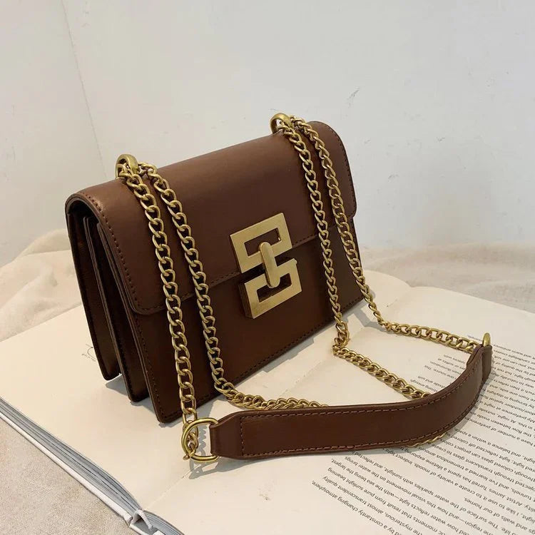 Brown leather shoulder bag with gold chain strap and geometric buckle on open book