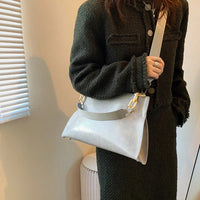 Woman wearing a dark textured coat holding a stylish light gray shoulder bag indoors