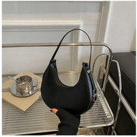 Black crescent shoulder bag on metal rack, modern minimalist interior, coffee cup nearby