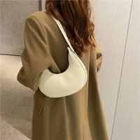 Woman in brown coat carrying white crescent shoulder bag, modern minimalist style