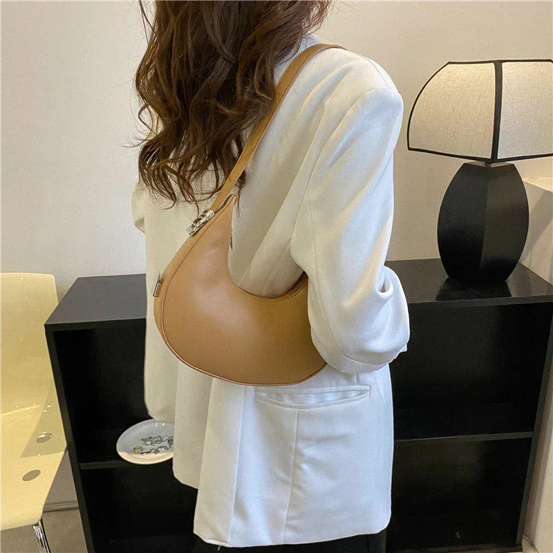 Woman wearing a white blazer and tan shoulder bag in a modern room with a black lamp