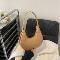 Tan crescent shoulder bag on black chair, modern minimalist handbag style