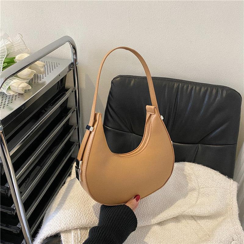 Tan crescent shoulder bag on black chair, modern minimalist handbag style