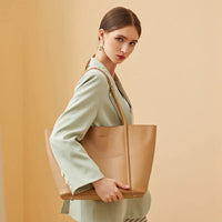 Woman in light green blazer holding large tan leather tote bag on beige background