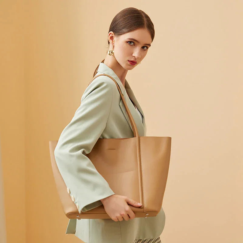 Woman in light green blazer holding large tan leather tote bag on beige background