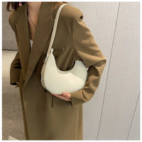 Woman in brown blazer holding minimalist white crescent shoulder bag