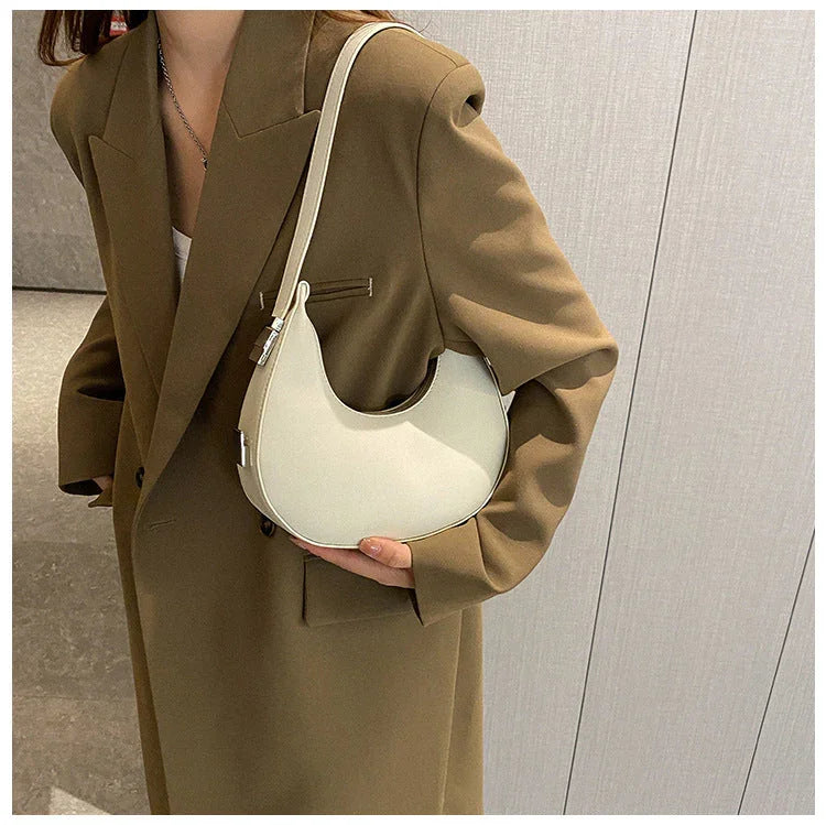 Woman in brown blazer holding minimalist white crescent shoulder bag