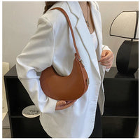 Woman in white blazer holding brown crescent shoulder bag in modern interior