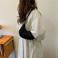 Woman in cream coat with black shoulder bag stands by wooden desk