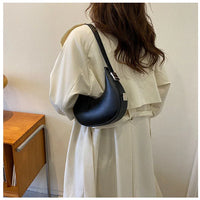 Woman in beige trench coat with black crescent shoulder bag indoors