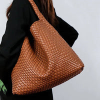 Woman carrying large woven brown leather tote bag over shoulder