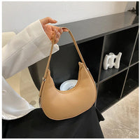 Woman holding beige crescent shoulder bag in modern minimalist room with black shelving