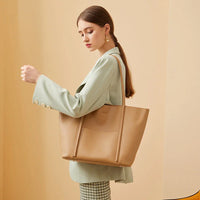 Woman in mint blazer carrying large tan leather tote bag against beige background