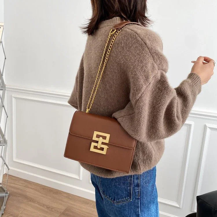 Woman wearing a brown crossbody purse with gold chain strap and geometric clasp, casual outfit