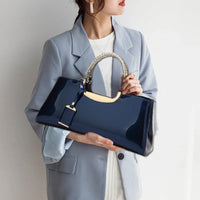 Woman in light blue blazer holding glossy navy blue handbag with braided handle