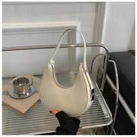 White crescent shoulder bag on metal shelf, minimalist modern purse with handle