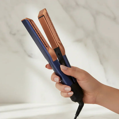 Hand holding a blue and brown hair straightener against a neutral background