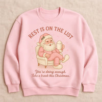 Pink sweatshirt with Santa Claus graphic and text on a beige background