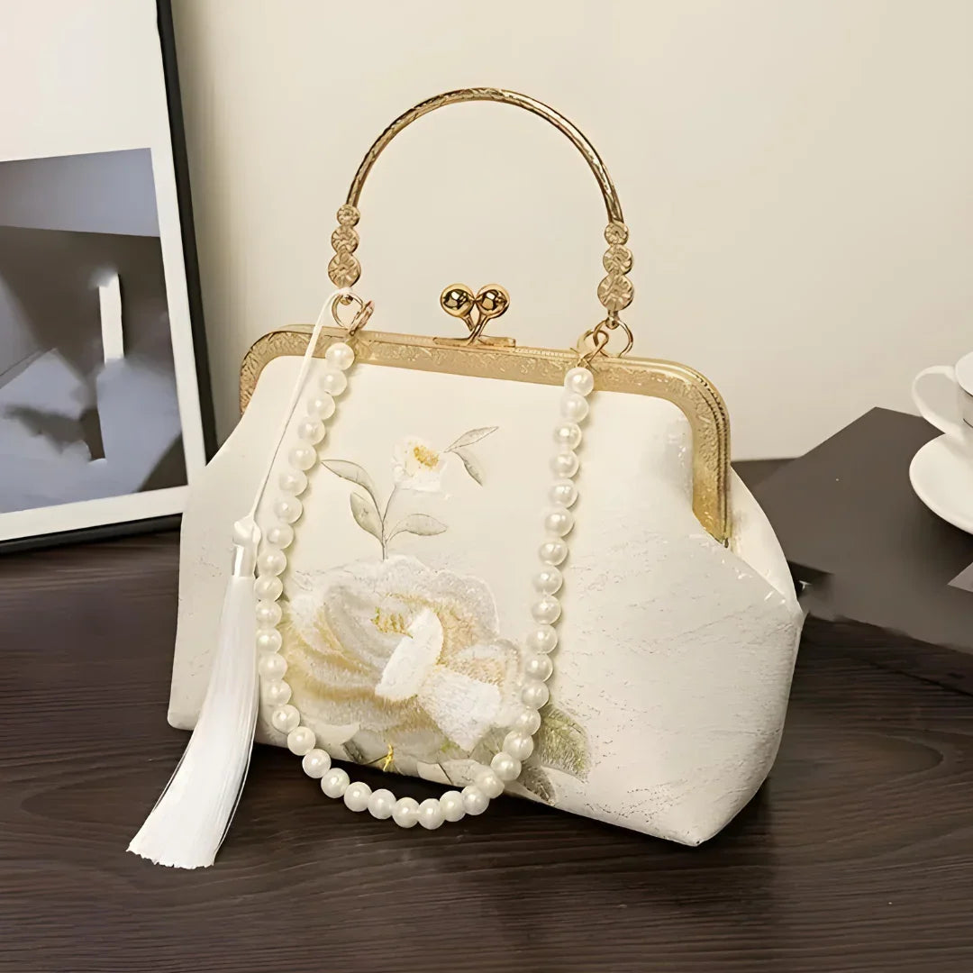 Elegant white floral embroidery handbag with pearl handle on dark wooden table