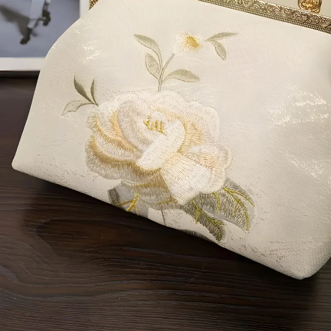 Elegant floral embroidered white clutch bag on dark wood surface