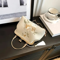 Elegant white floral embroidered handbag with gold handle on black cabinet