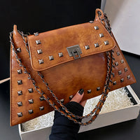 Brown leather studded handbag with chain strap, held above a white gift box
