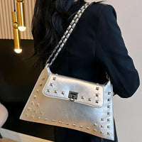 Woman in black outfit holding silver studded shoulder bag with chain strap