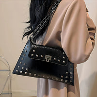 Woman in beige coat with black studded leather shoulder bag and chain strap