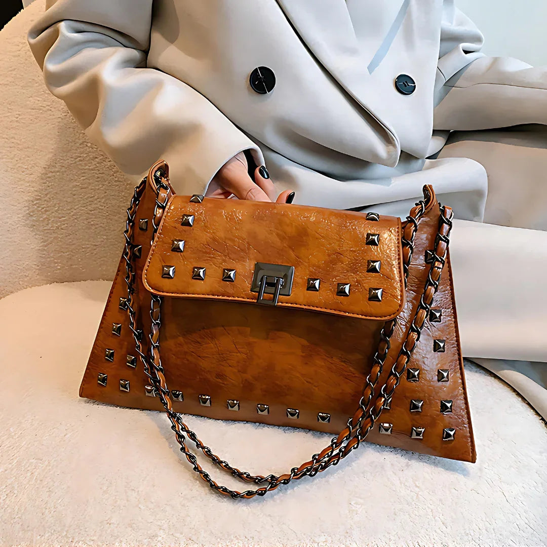 Brown leather studded handbag with chain strap on woman's lap in beige coat