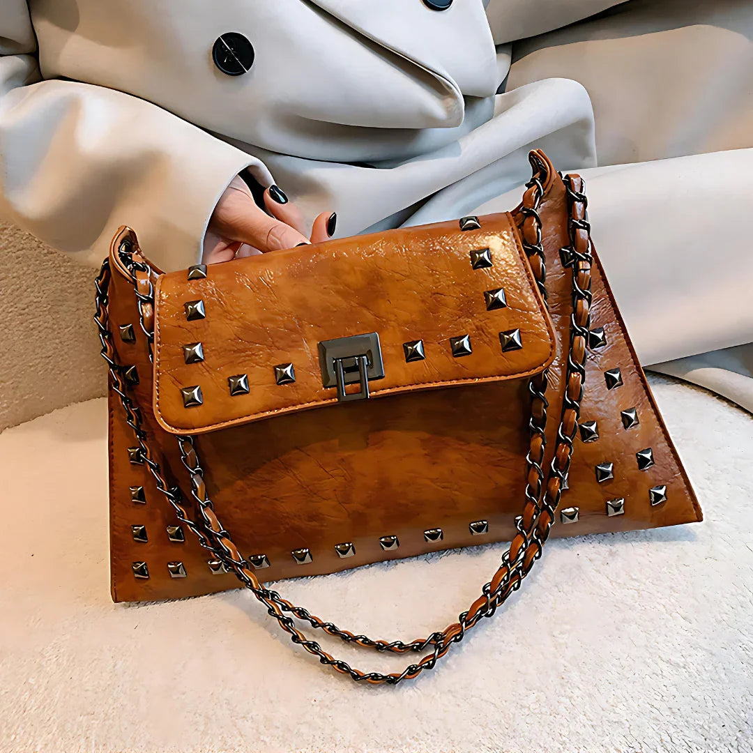 Brown leather studded handbag with chain strap and silver clasp, woman in beige coat