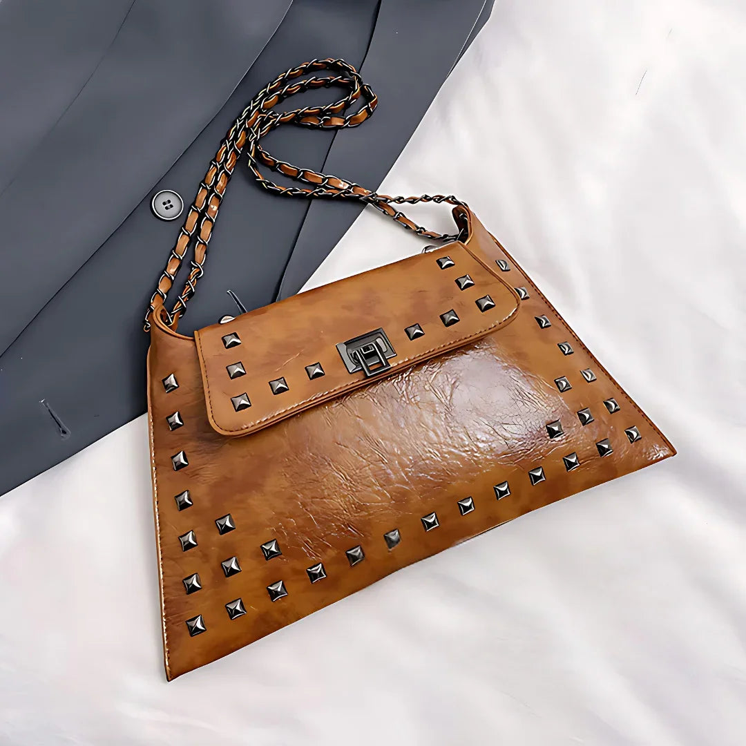 Brown leather studded clutch bag with chain strap on white and gray fabric background