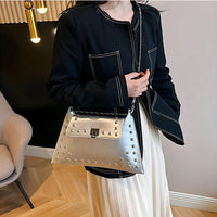 Woman in black jacket holding metallic studded handbag indoors