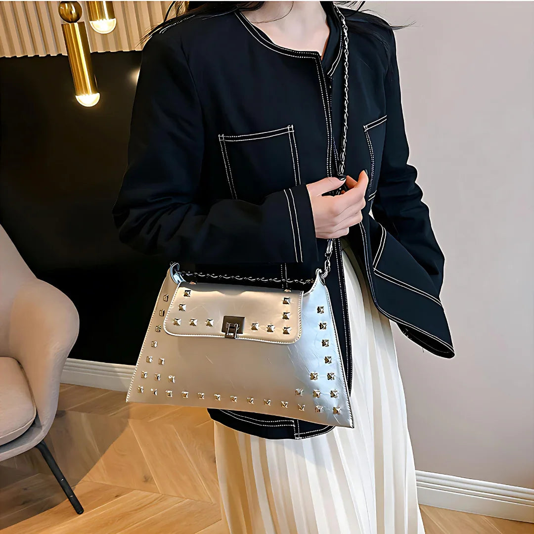Woman in black jacket holding metallic studded handbag indoors