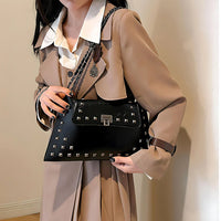 Woman in beige trench coat holding black studded shoulder bag indoors
