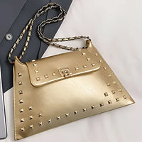 Gold studded leather handbag with chain strap on a white and grey surface